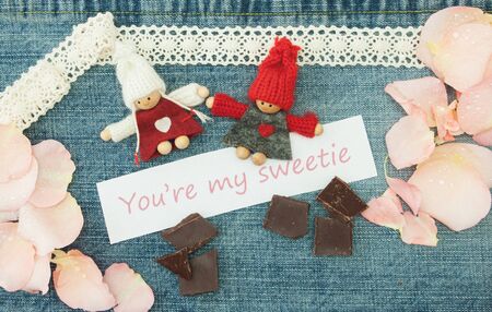 Valentine, greeting card with knitting couple in love, pieces of chocolate and soft pink rose petals.の写真素材
