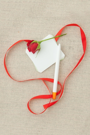 Valentine, greeting card with red little rose, pen, blank and red ribbon in the shape of a heart.の写真素材