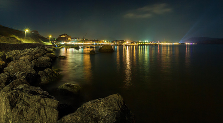 panorama, horizontal view of Crimean mountains with rocky coastline of Black sea with city lights on the background.Night luminous embankmentの写真素材