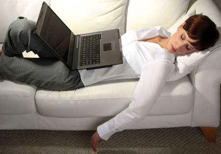 Young business woman sleeping on sofa, laptop resting on stomach の写真素材