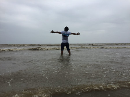 a boy standing with arms wide open in the waters of the sea under the blue sky