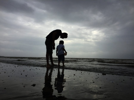 a father and a son silhouette at a sea beach with dark blue sky