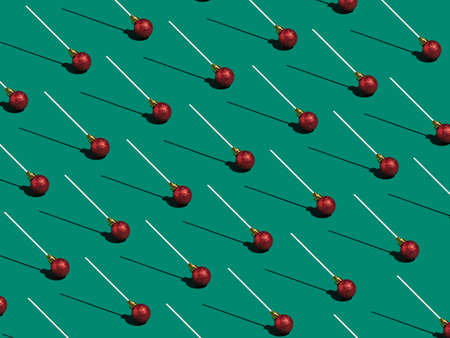 Lollipop made of red Christmas bauble on green background. Christmas sweets concept. Christmas isometric pattern, background, banner.の写真素材