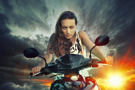 Emotional portrait of young beautiful woman on a motorbike on the background of dark sky の写真素材