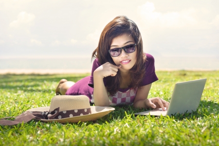 Pretty young asian woman is dreaming with a laptop lying on the grass の写真素材