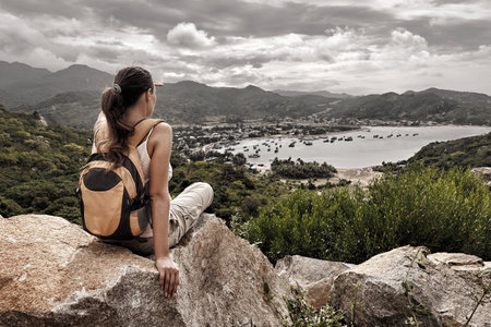 Woman traveler looks at the edge of the cliff on the  sea bay of mountains in the backgroundの写真素材