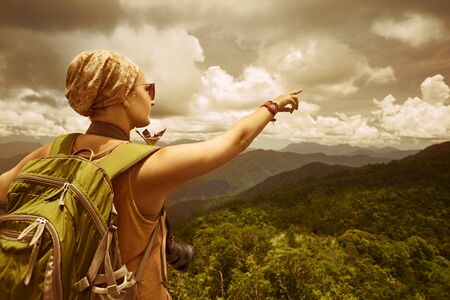 Portrait of happy young traveler woman with backpack standing on top of the mountain and enjoying valley view with raised hand.
Travel to Asia, happiness emotion, summer holiday conceptの写真素材