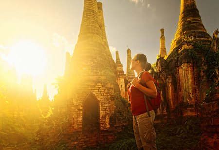 Woman backpacker traveling with backpack and looks at sunset ancient Buddhist stupa of the temple complex In Dein, Inle Lake. MayanmarTraveling along Birma, freedom and active lifestyle conceptの写真素材