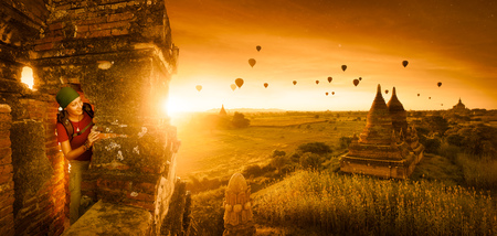Woman traveler with a backpack explores the ancient temple on a background of beautiful sunrise with balloons. Bagan, Myanmar.Traveling along Asia, active lifestyle concept.の写真素材