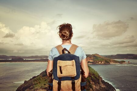 Happy traveler with a backpack, enjoying the view of a tropical coast on a background the mountains.Young backpacker traveling along Asia, happy female walking discovering world, summer vacation conceptの写真素材