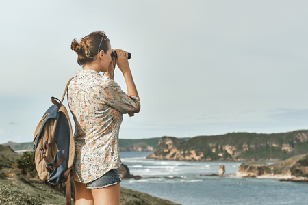 Happy young woman tourist with backpack enjoying sunny coast view on sunrise.
Traveling along mountains and coast, freedom and active lifestyle concept.の写真素材