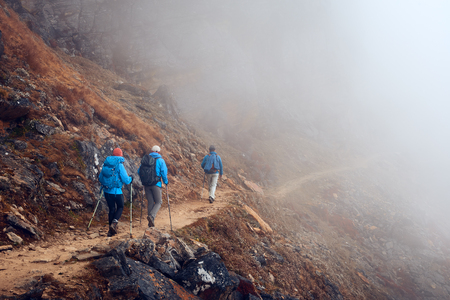 Group Hikers with Backpacks walking down on Mountain Trail enjoying on view of foggy mountains. 
Mountains and landscape, travel , happiness emotion, summer holiday concept
