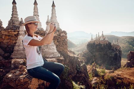 young woman traveller photographs landscape and stupas in the temple complex Main May' Tha-Khin-Ma Mountain. Myanmar(Burma), Asia. 
Traveling along Asia, travel and adventure lifestyle concept.の写真素材