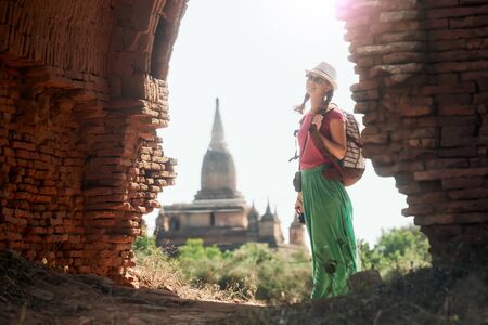 Positive emotions. Happy woman traveler with a backpack walking through the Old Bagan looking the ancient Buddhist ruins. Myanmar. Concept of travel and adventure in Asia.の写真素材