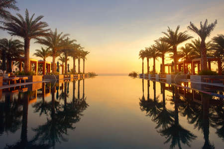 Beautiful view of sunrise at swimming pool. Luxurious tropical beach landscape, umbrellas and loungers and water reflectionの写真素材