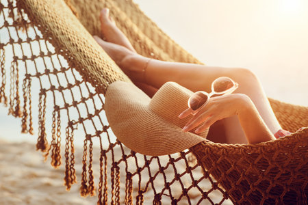 Feet and hand relaxing woman in hammock on the beach during sunset.の写真素材