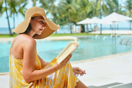 Vacation Beach Summer Holiday Concept. Beautiful woman reading book resting in luxury hotel in summer.の写真素材