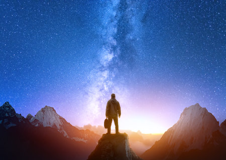 Silhouette of confident man standing on top of mountain with night sky and bright sunset light in background.の写真素材