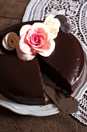 A whole dark chocolate cake with flowers decorations, a piece missing の写真素材