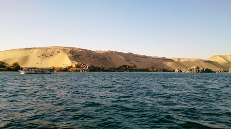 Large sand dunes on the banks of the Nile River, near Aswan. You can see a ferry and some vegetation...