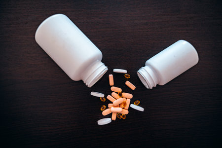 Two white jars with scattered red, pink and black medicines on a dark table.