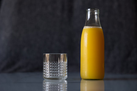 An empty glass next to a full bottle of orange juice.の写真素材