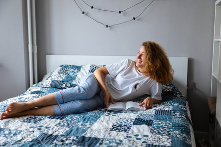 young woman reading book or studying lying home couch looking happy and relaxed.の写真素材