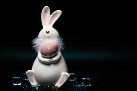 Sculpture of a white rabbit with Easter eggs on black background with ice cubesの写真素材