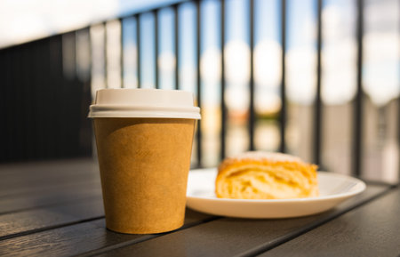 A paper cup of coffee with a white lid the table next the pie Cafe open veranda