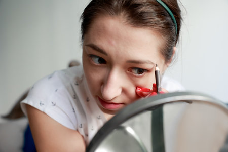 young girl paints eyebrows with pencil for expressive makeup Home makeup and self-care conceptの写真素材