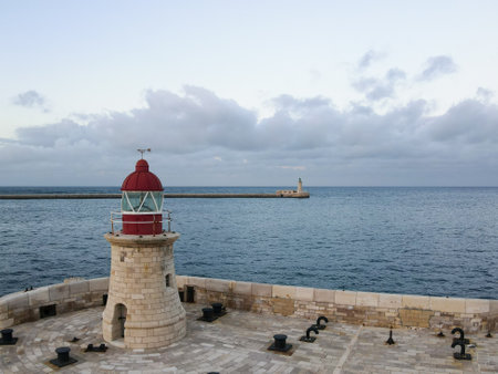 Scenic view of a red lighthouse on a stone pier with the ocean in the background. Maritime navigation and coastal landmark conceptの写真素材