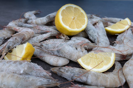 Fresh shrimp is scattered on the table with lemon slices. Products for grilling. Lemon slices and frozen shrimpの写真素材
