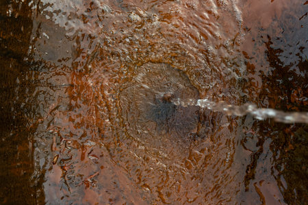 A thin stream of water pours onto the water surface. Circles on the water.