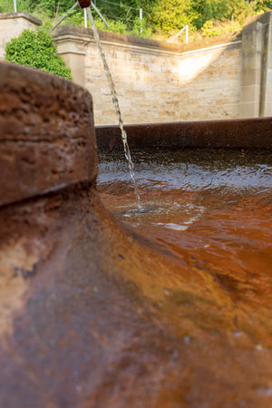 Drinking water pours from the tap on the street. An old rusty faucet from which water runs into a water tankの写真素材