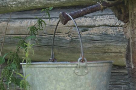 the bucket hangs on the wall of a wooden sauna on a rusty nail, a summer village lifeの写真素材