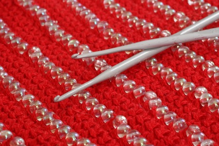 crochet hook on the knit cloth of red color with decoration of beads, red backgroundの写真素材