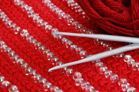 crochet hook on the knit cloth of red color with decoration of beads, red backgroundの写真素材
