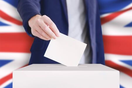 Man putting a ballot into a voting box with British flag on background.の写真素材