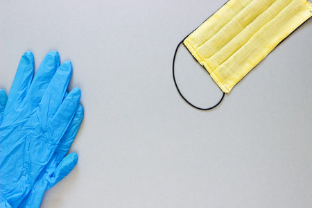 Yellow medical mask and blue gloves to protect health from the virus on a gray background