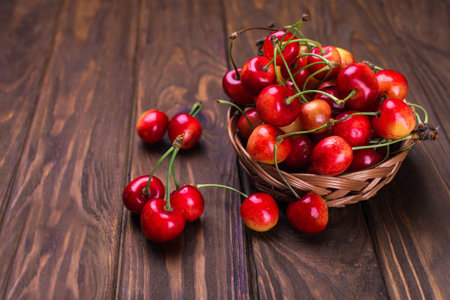 Ripe yellow and red cherries on wooden table with in a basketの写真素材