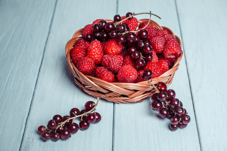 Red currant and raspberry in a basket on a white wooden background, close-up