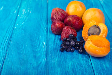 Fresh apricots, blueberris and strawberries on wooden turquoise background.の写真素材