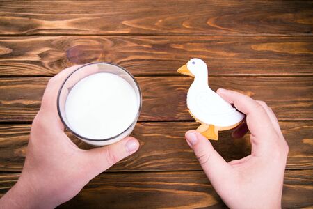 Closeup of mans hands holding glass of milk and homemande gingerbrad duck shaped cookie on a wooden backgroundの写真素材