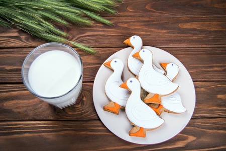 Tasty gingerbread suck shaped cookies on a white plate with part og a milk glass and with ear of wheat on a brown wooden backgroundの写真素材