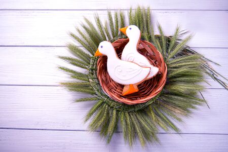 Two duck shaped ginger cookies with basket nest  wreath with spikelets top view on a white wooden background. Toned picture.の写真素材