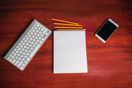 Notepad with  keyboard,mobile phone and pencils on wooden backgroundの写真素材