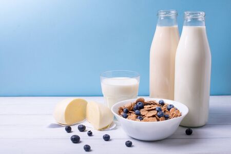Front view of fresh dairy products (mozzarela and milk) and cereals with blueberries on a white wooden table and blue background. Shallow depth of fieldの写真素材