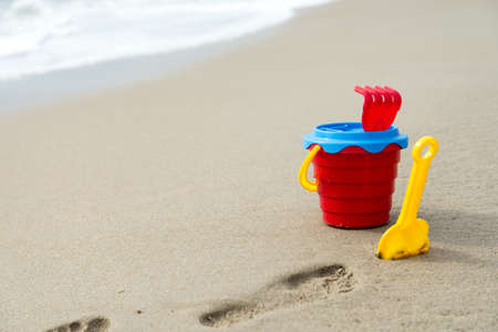 Red bucket with a shovel, a rake and a net on the beach and wet sandの写真素材