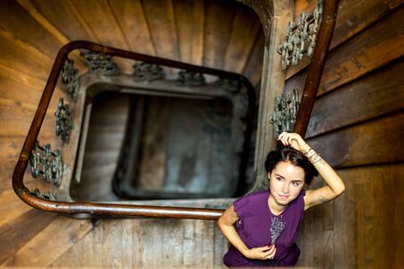 Portrait of a girl in romantic style lying on a banisters at spiral staircase in a ray of light, with tatoo and with lavender at her hand. Dark interior. Copy space.の写真素材