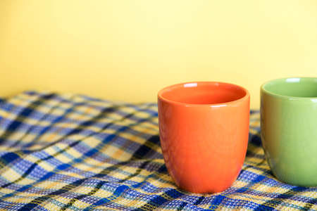 One orange mug and half of green mug standing on a waffle blue towel on a yellow backgroundの写真素材